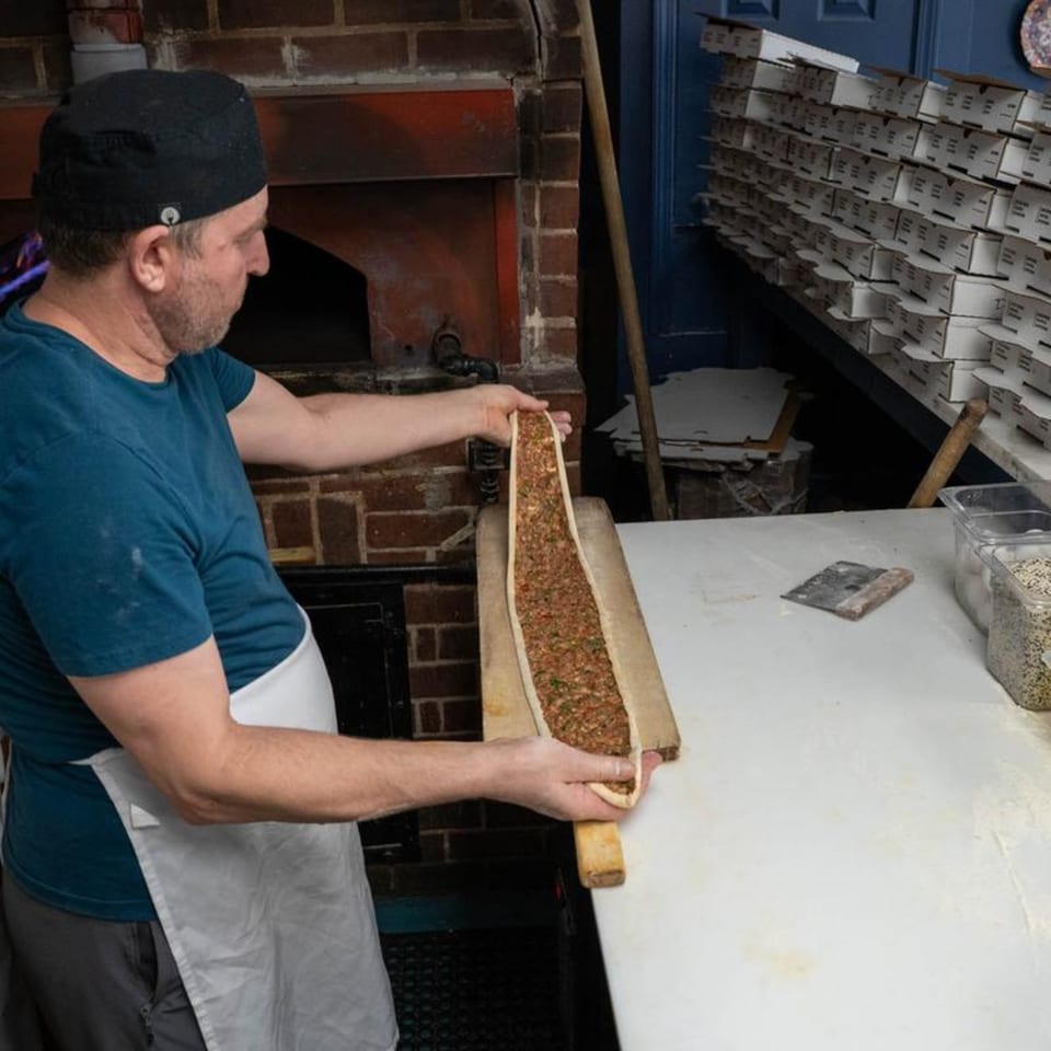 Chef at Istanbul Grill Metairie preparing a long, thin Mediterranean pastry filled with ground meat.