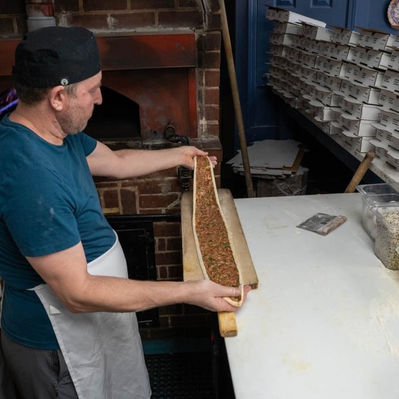 Chef at Istanbul Grill Metairie preparing a long, thin Mediterranean pastry filled with ground meat.