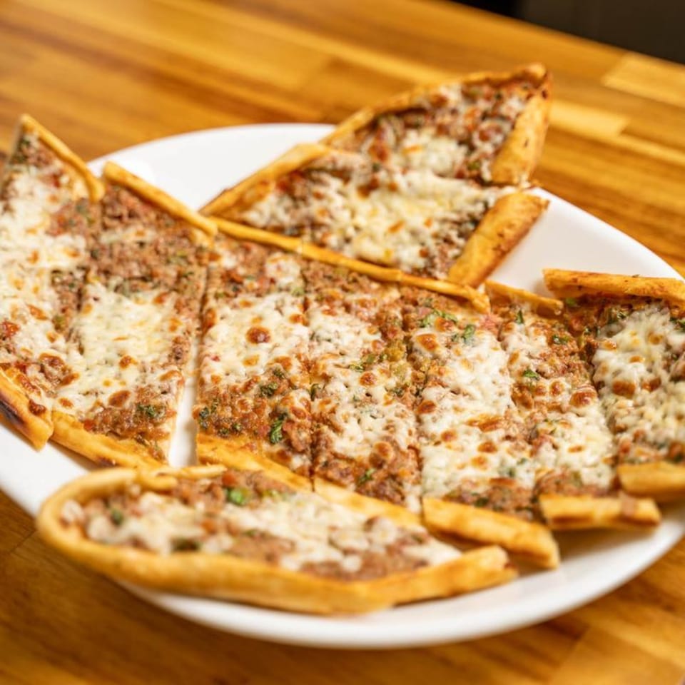 A white plate filled with several slices of Turkish Pide, topped with ground meat and melted cheese.