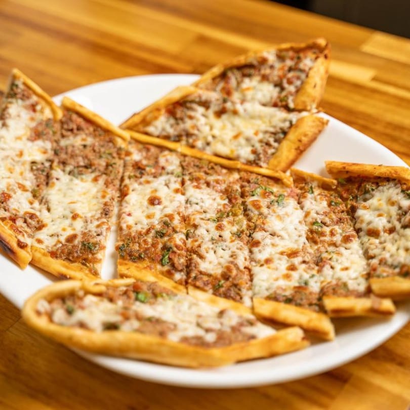 A white plate filled with several slices of Turkish Pide, topped with ground meat and melted cheese.
