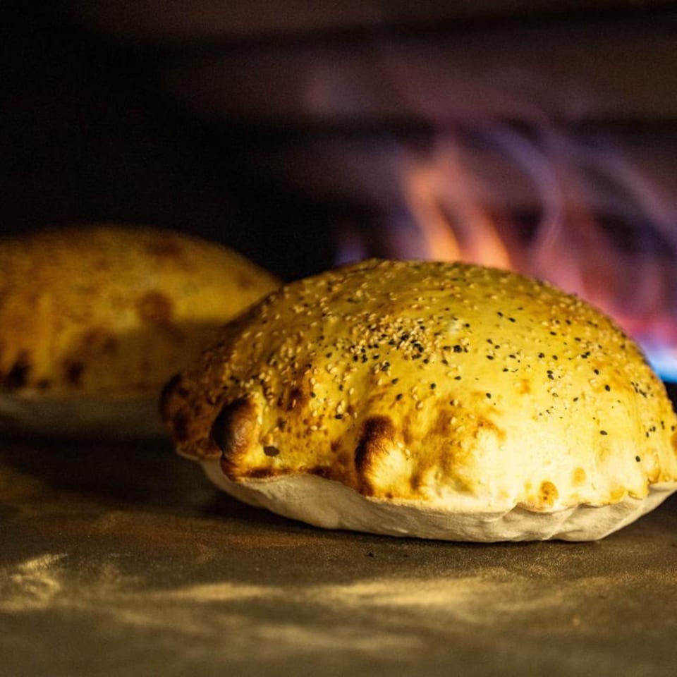 Freshly baked, golden-brown pita bread with sesame seeds cooking in a fiery oven.