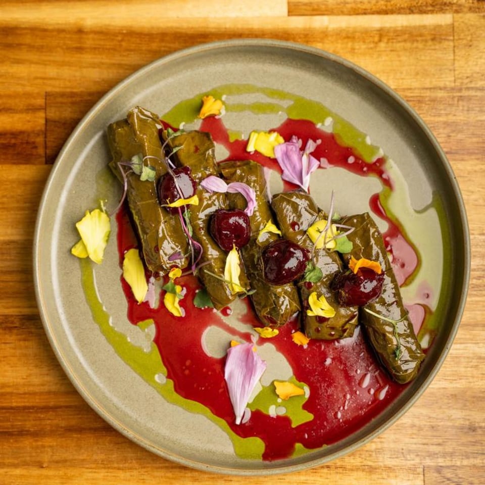 Mediterranean dolmas with red and green sauces, garnished with edible flowers on a plate.