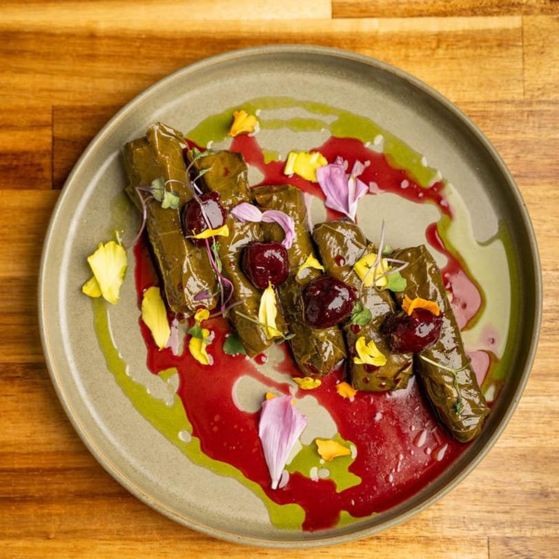 Mediterranean dolmas with red and green sauces, garnished with edible flowers on a plate.