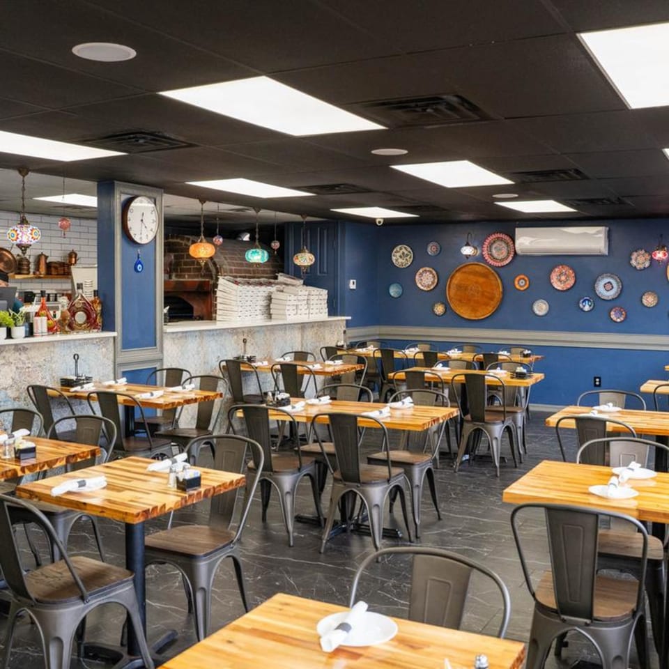 Interior of ISTANBUL GRILL METARIE, featuring wooden tables, metal chairs, and decorative plates on blue walls.