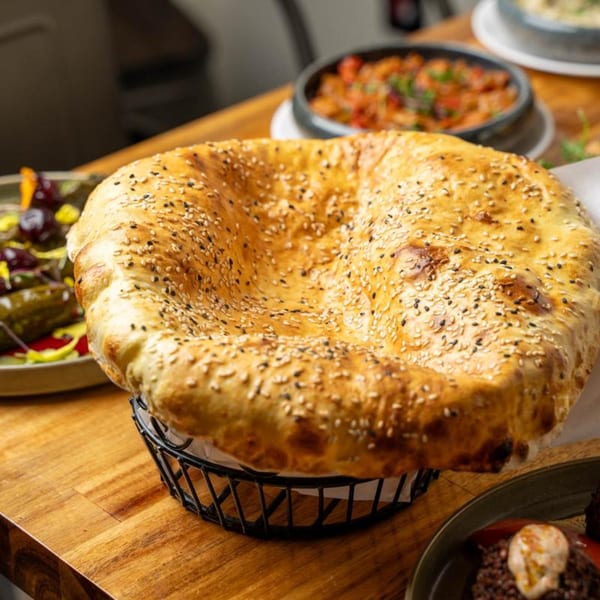 Freshly baked, sesame-crusted Mediterranean bread in a basket, with other dishes blurred in the background.