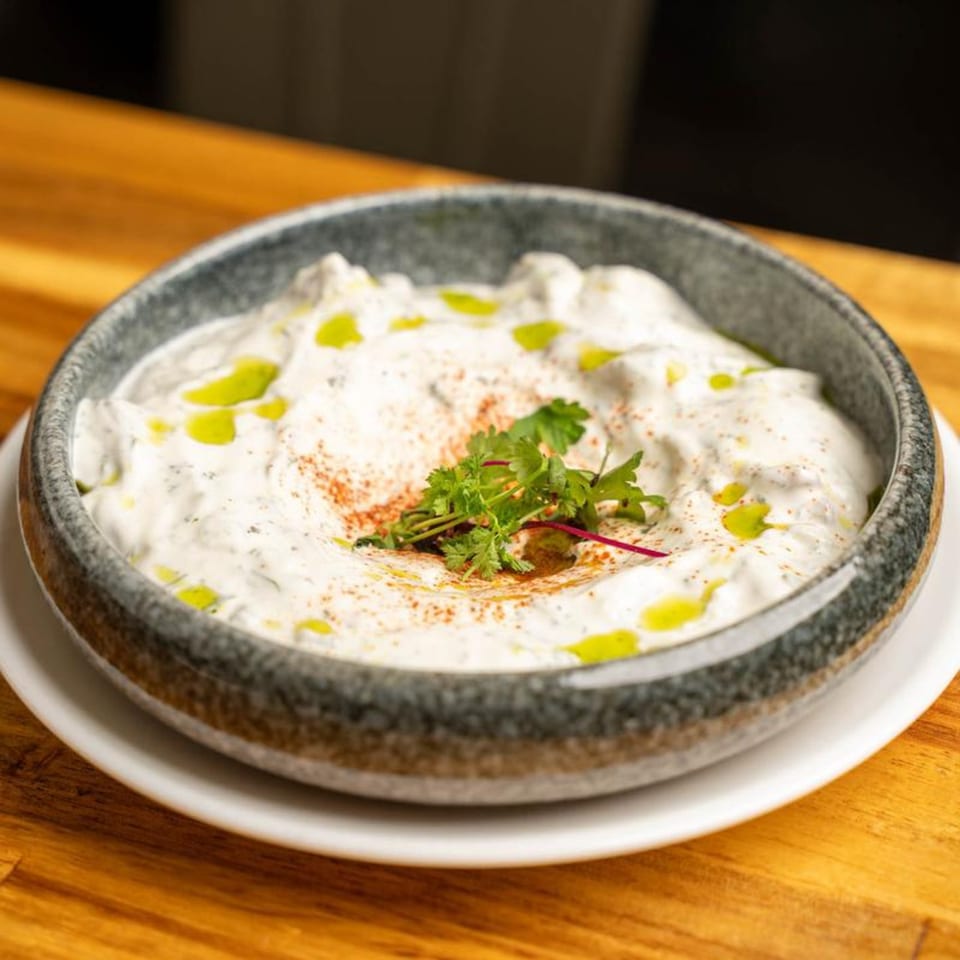 A bowl of creamy Mediterranean dip, garnished with herbs, paprika, and olive oil, on a wooden table.