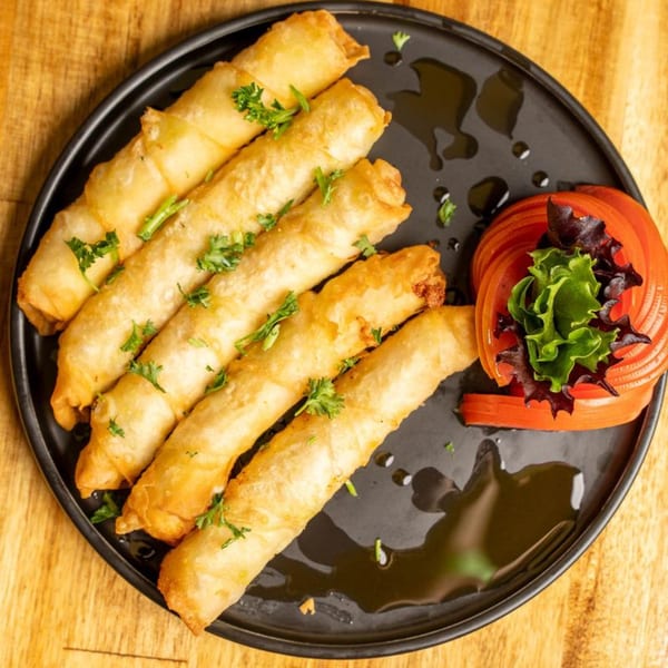 Five golden-brown fried spring rolls garnished with parsley, served with sliced tomatoes and lettuce.