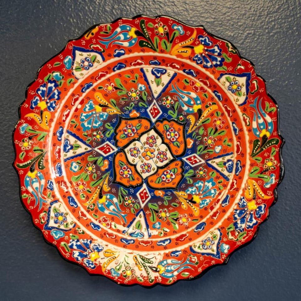 A vibrant, ornate Mediterranean decorative plate with intricate floral patterns in red, blue, green, and yellow.