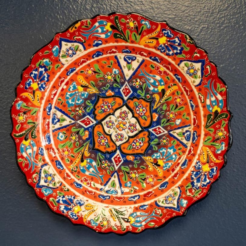 A vibrant, ornate Mediterranean decorative plate with intricate floral patterns in red, blue, green, and yellow.