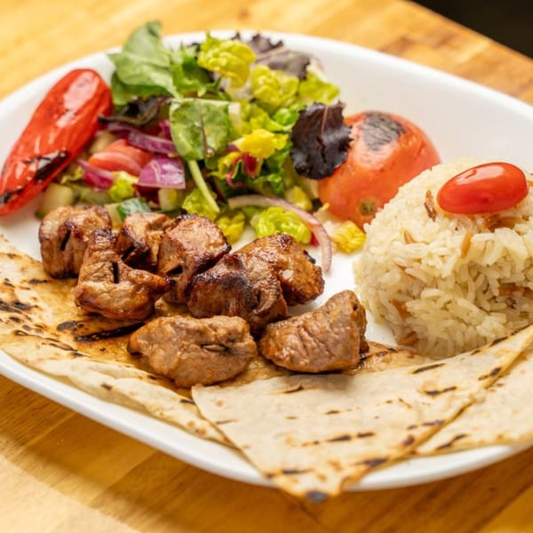 Mediterranean shish kebab with rice, salad, grilled pepper, and tomato on a white plate.