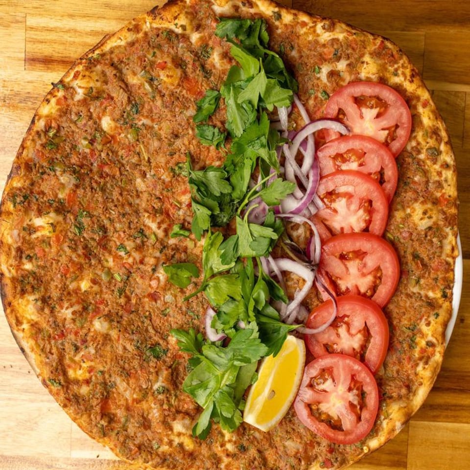 Lahmacun, a Turkish flatbread pizza, topped with minced meat, parsley, red onions, tomatoes, and a lemon wedge.
