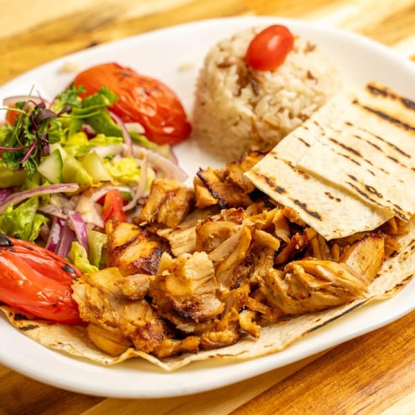 Chicken shawarma with rice, salad, grilled tomatoes, and flatbread on a white plate.