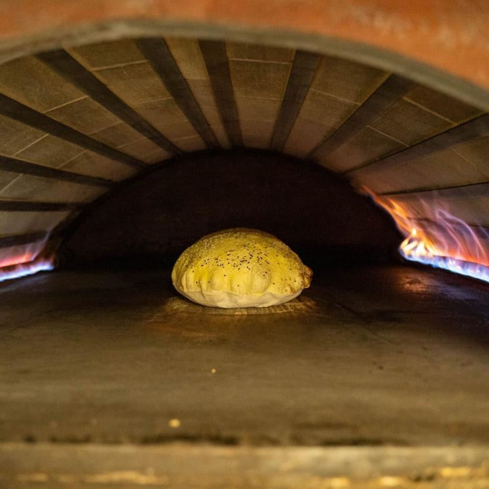 Pita bread baking in a brick oven with flames visible on both sides.