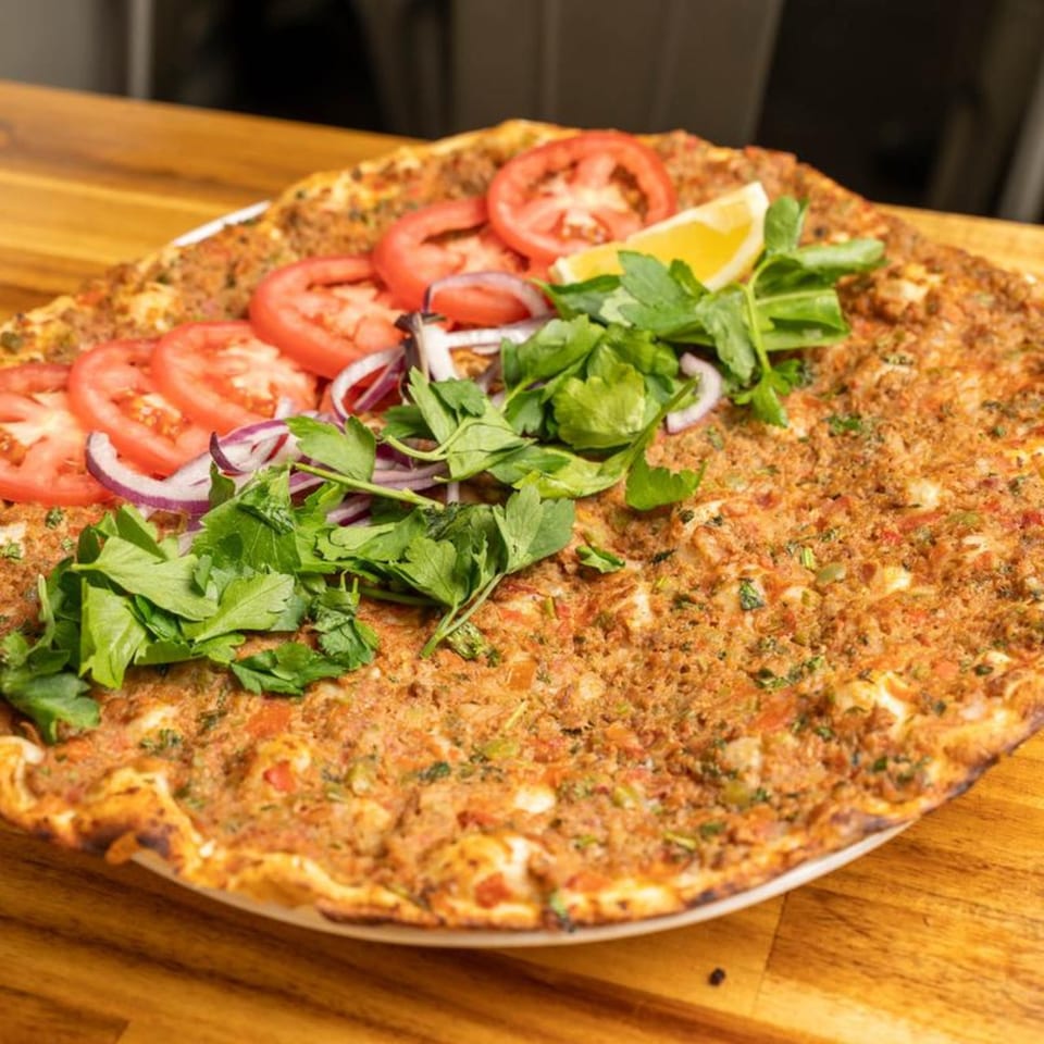 Lahmacun, a Turkish flatbread pizza, topped with tomatoes, red onions, parsley, and a lemon wedge.