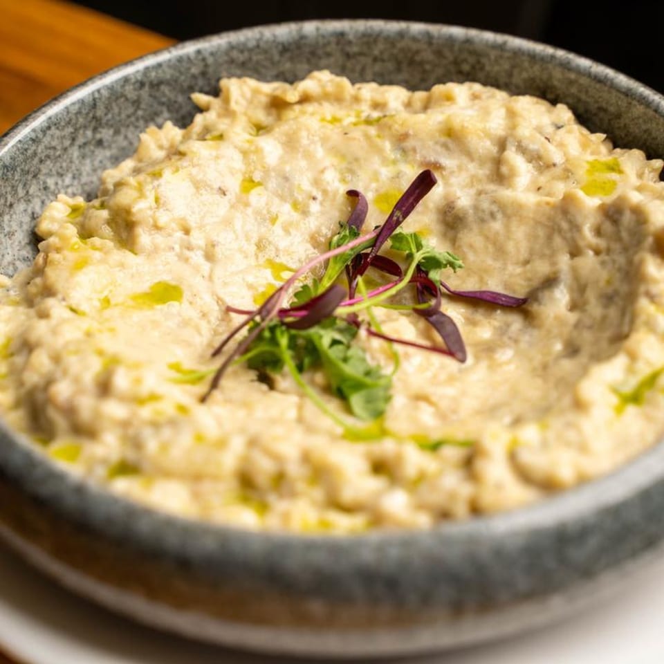 Creamy Mediterranean baba ghanoush, drizzled with olive oil and garnished with fresh herbs in a gray bowl.