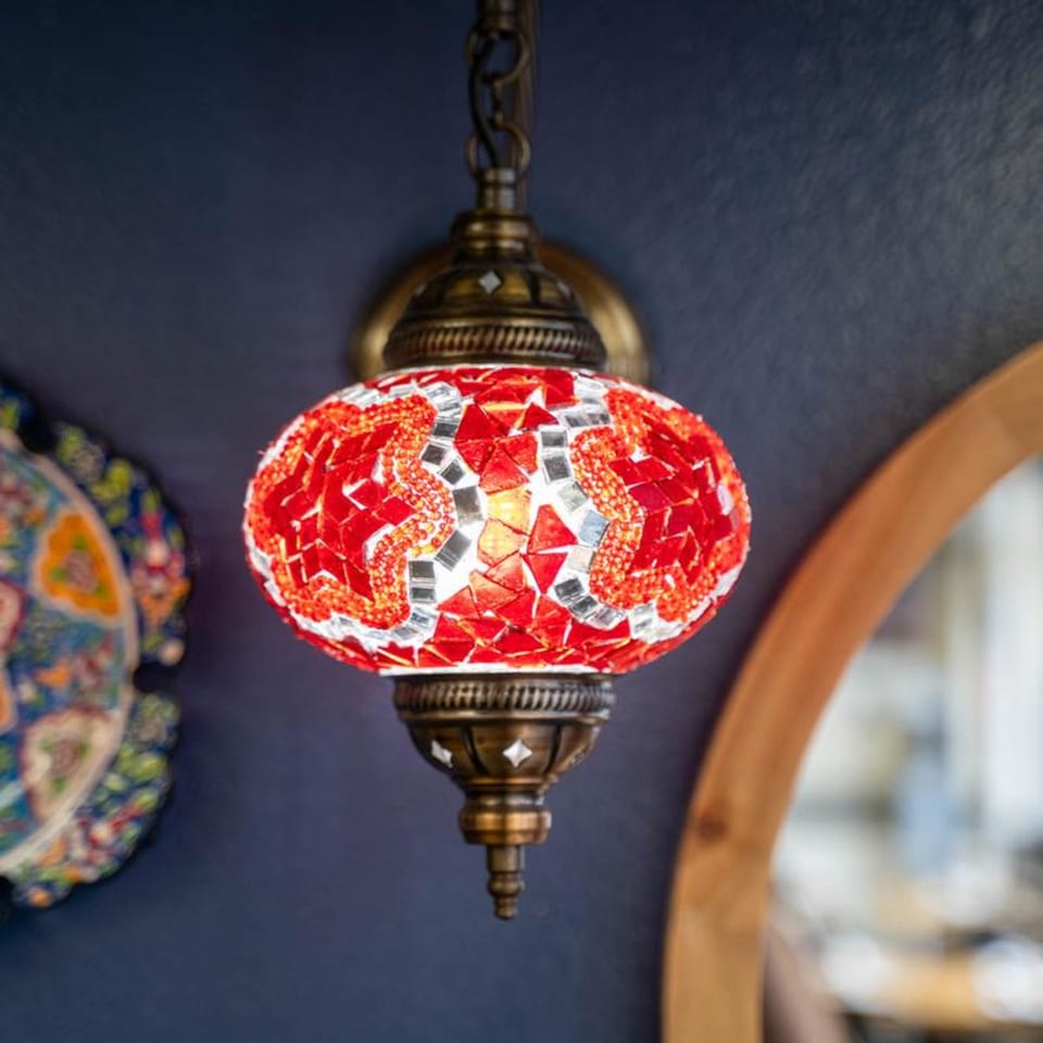 A vibrant red and white mosaic Turkish lamp hangs against a dark blue wall.