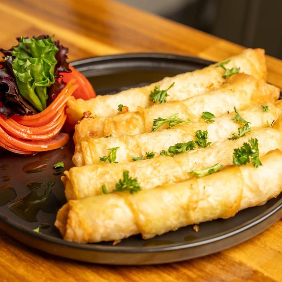 Golden fried cheese rolls, garnished with parsley and a side of fresh salad on a black plate.