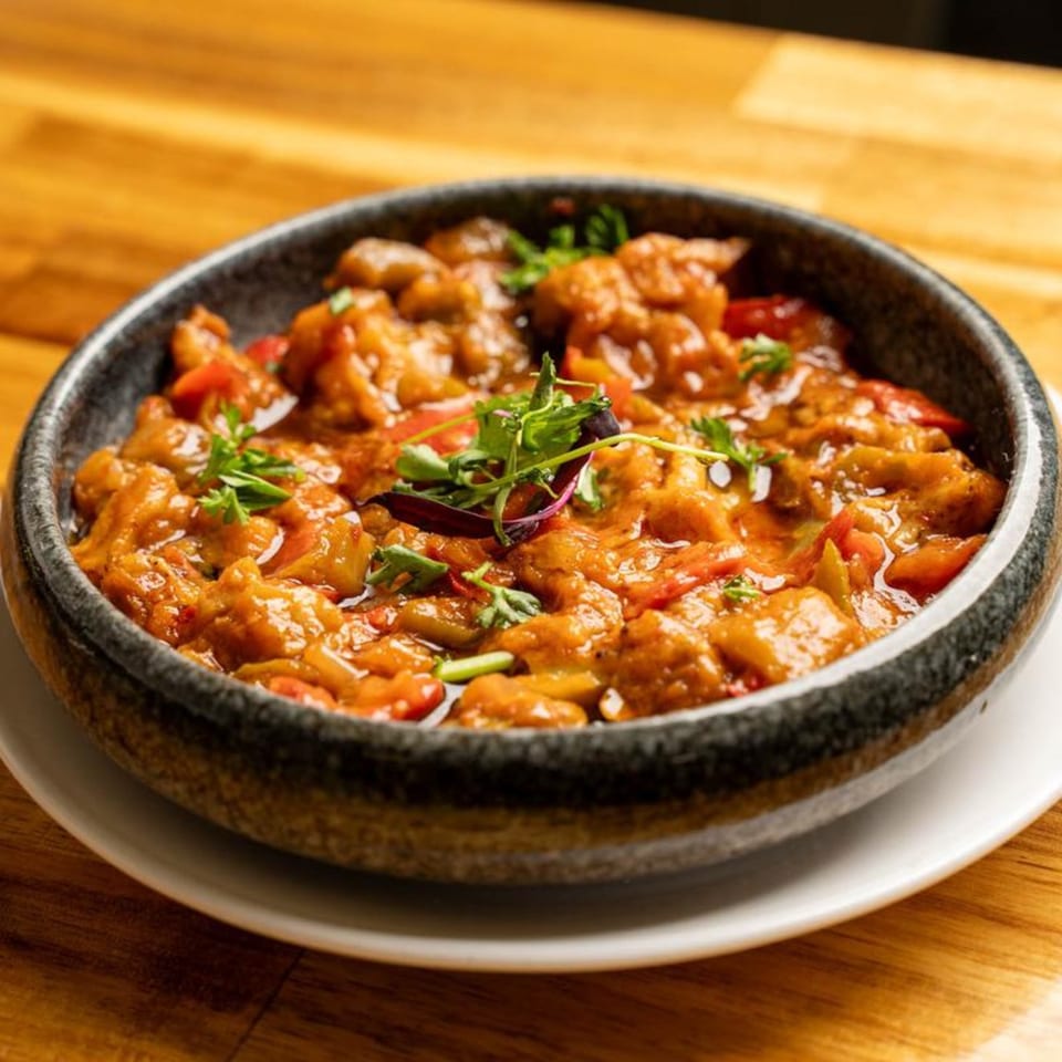 A Mediterranean dish with chunky orange sauce, red peppers, and green herbs in a dark bowl.