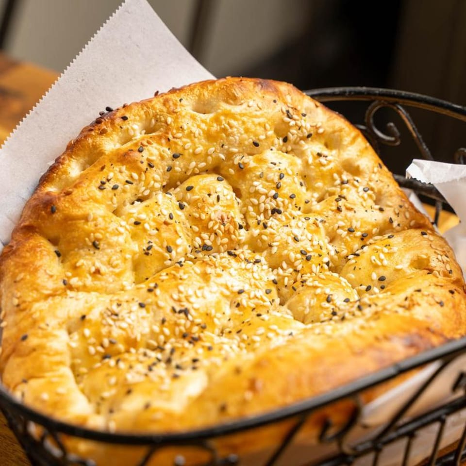 Freshly baked Mediterranean flatbread, topped with sesame seeds, served in a black wire basket.