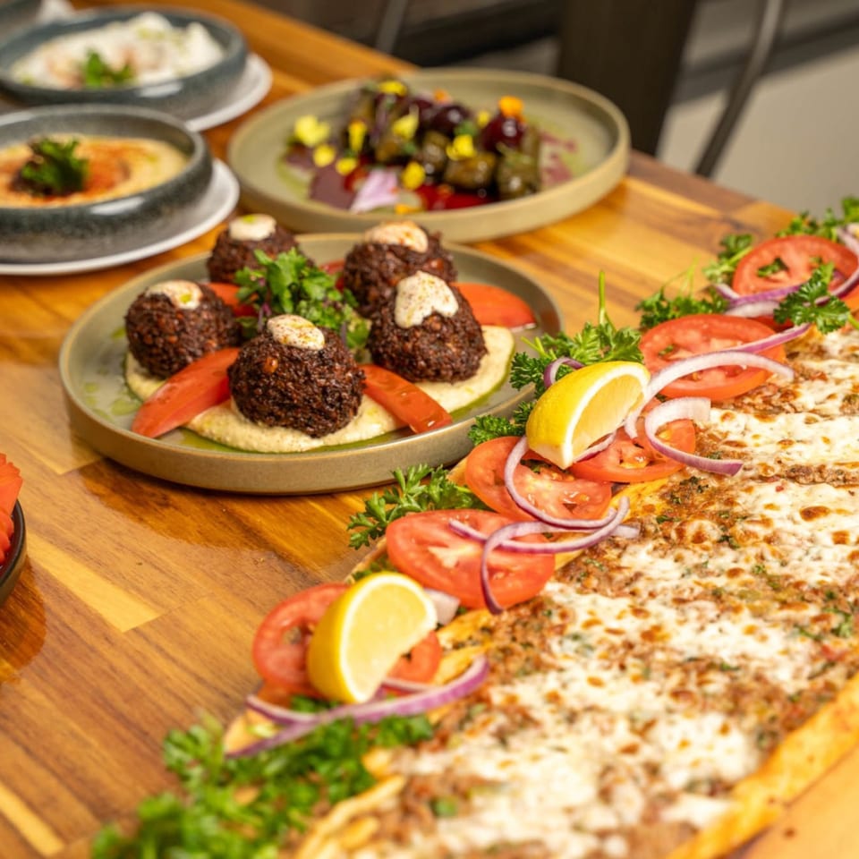 A wooden table laden with various Mediterranean dishes, including falafel, hummus, and a long flatbread.