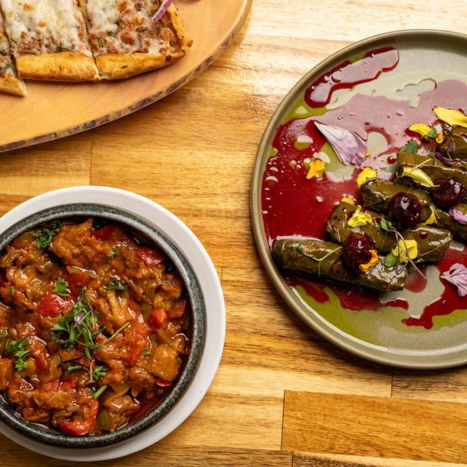 A Mediterranean spread featuring a flatbread, a stew, and dolmas with cherry sauce and edible flowers.