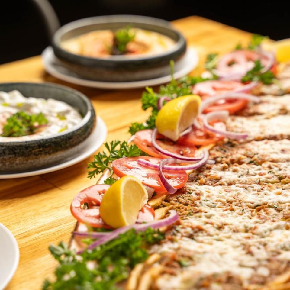 Lahmacun, a Turkish flatbread, garnished with tomatoes, red onions, parsley, and lemon wedges.