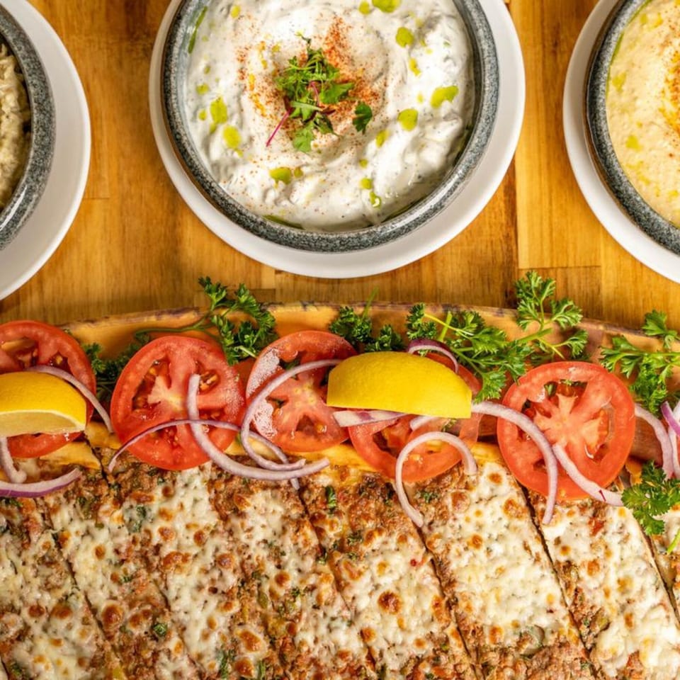 Mediterranean flatbread with melted cheese, tomatoes, onions, lemon, and parsley, served with dips.