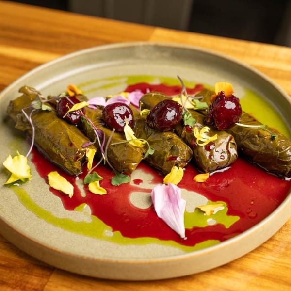Mediterranean dolmas with cherry sauce, green drizzle, and edible flower petals on a plate.