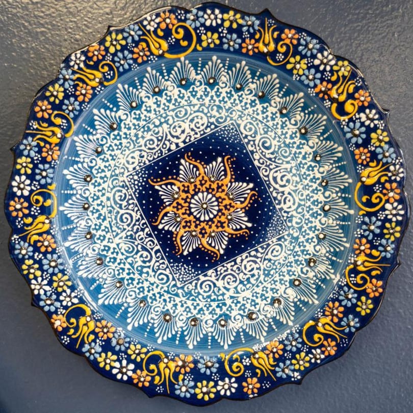 A decorative blue and white Mediterranean plate with intricate floral and geometric patterns in yellow and orange.
